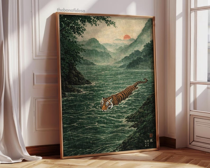 May include: A framed art print showing a tiger swimming in a river, with mountains and a setting sun in the background. The artwork is in a traditional Japanese style, with muted greens, browns, and oranges. The frame is gold.