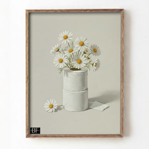 May include: A framed print depicting a still life of daisies in a white, textured container made of stacked toilet paper rolls. A single daisy and a torn piece of paper are on the light grey surface. The frame is light brown.