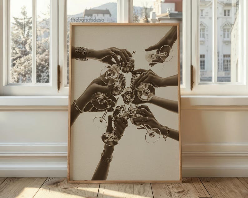May include: Sepia-toned print of hands holding champagne glasses in a celebratory toast. The image is framed in a light wood frame and set against a neutral background. The text "thebonafideso" is visible in the upper left corner.