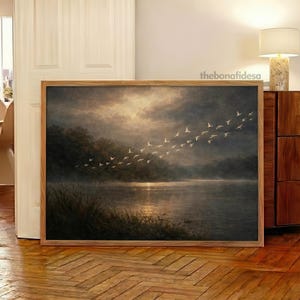 May include: A framed landscape painting depicts a serene lake scene with a flock of birds in flight. The artwork features a wooden frame and a muted color palette, with a focus on the water and sky. The text "thebonafidesa" is visible in the top right corner.