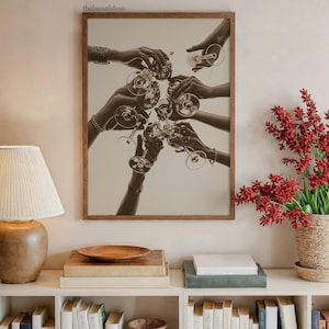May include: Sepia-toned framed print featuring a celebratory toast with wine glasses. Multiple hands are raised, holding the glasses in a clinking gesture. The image is set against a neutral background, creating a classic and elegant aesthetic.