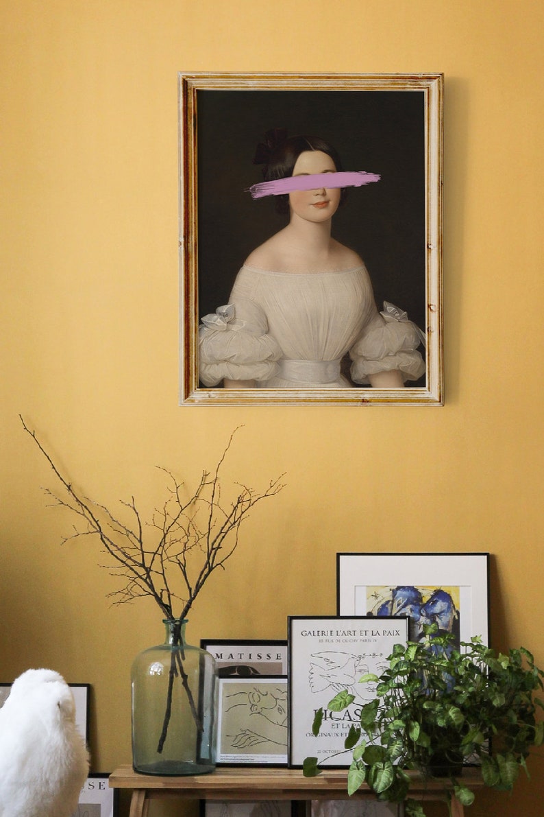 May include: A framed portrait of a woman in a white dress with a pink brushstroke covering her eyes. The portrait is hanging on a yellow wall with other framed artwork and a vase with branches.