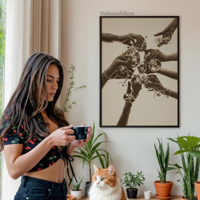 May include: A framed sepia-toned print depicts hands toasting with wine glasses. A woman in a black top with a cherry pattern holds a black mug. A ginger and white cat sits on a shelf with potted plants.