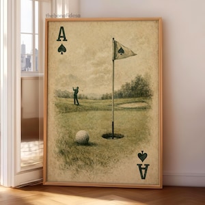 May include: A framed vintage-style print featuring a golf scene. The artwork depicts a golfer, a golf ball, and a flag on a green. The print also includes the Ace of Spades card suit symbols and text. The frame is made of wood.