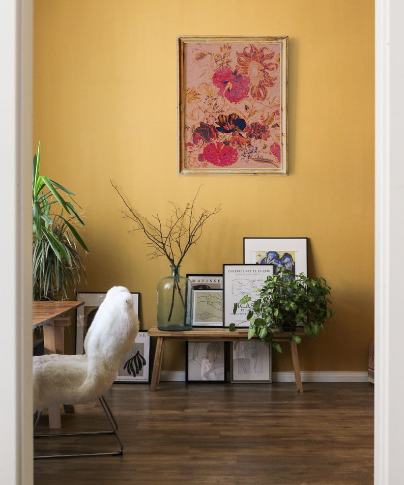 May include: A yellow wall with a framed floral print, a wooden bench with framed prints, a white furry chair, and a potted plant.