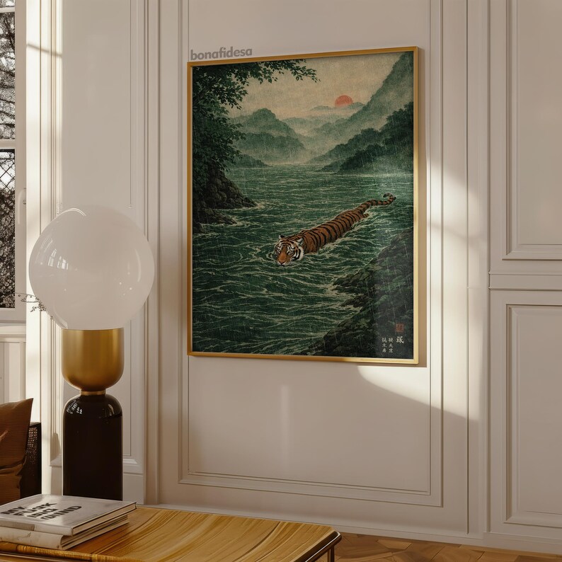 May include: A framed print depicting a tiger swimming in a river, inspired by Japanese art. The artwork shows a tiger with orange and black stripes in a green river, with mountains and a sunset. The frame is gold.