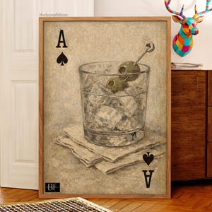 May include: A framed art print showing a cocktail glass with ice and olives, resting on napkins. The Ace of Spades card symbol is visible. The artwork has a neutral background and is presented in a wooden frame.