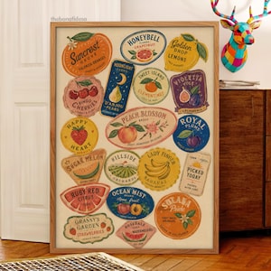 Op de afbeelding: Een ingelijste kunstdruk met een verzameling fruitkistetiketten in vintage-stijl. De etiketten tonen diverse vruchten zoals sinaasappels, kersen, peren, perziken, pruimen, bananen en aardbeien met teksten zoals Suncrest, Honeybell en Peach Blossom.