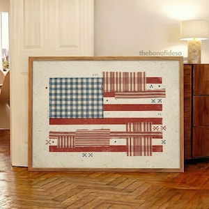 May include: A framed artwork featuring a patchwork design of the American flag. The flag incorporates various patterns, including gingham and stripes, in shades of blue, red, and white. The artwork is displayed in a natural wood frame.