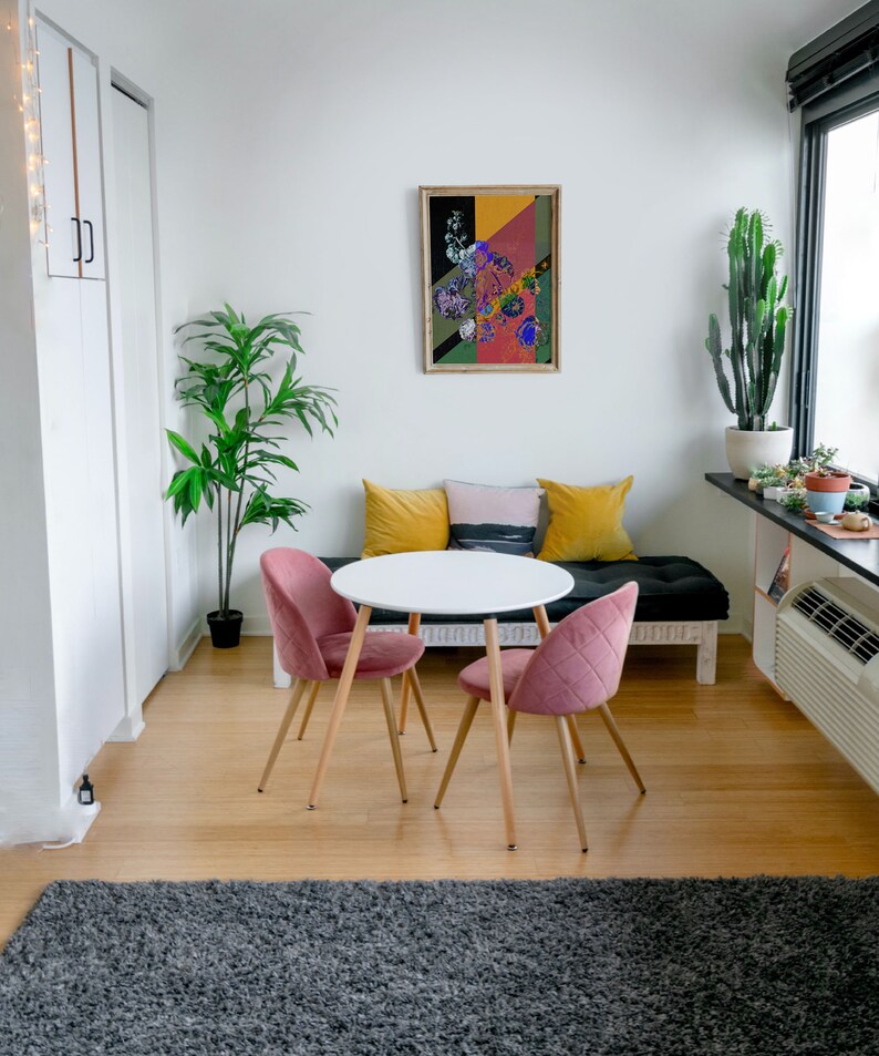 May include: A small dining area with a white round table and four pink chairs. The table is set with a gray rug underneath. There is a couch with yellow and gray pillows in the background.