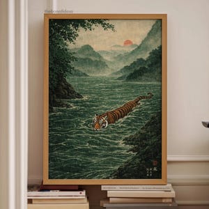 May include: A framed art print showing a tiger swimming in a river, with mountains and a setting sun in the background. The artwork has a vintage aesthetic, with a colour palette of greens, browns, and oranges. The print is in a wooden frame.