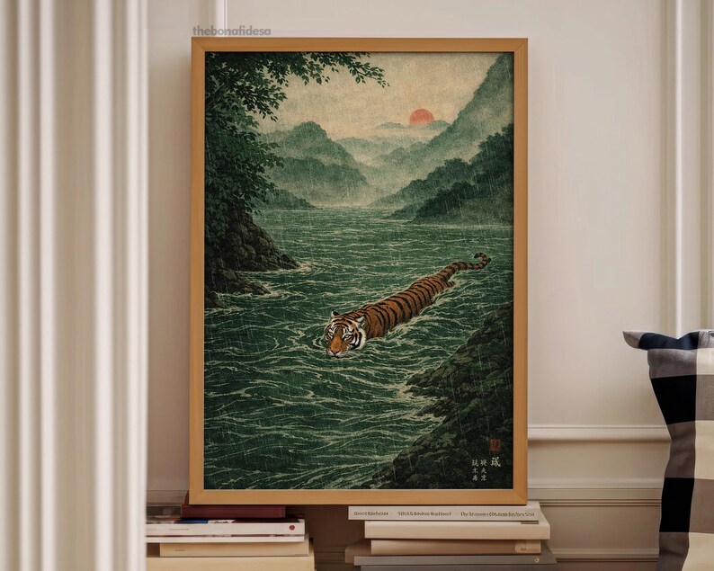 May include: A framed art print showing a tiger swimming in a river, with mountains and a setting sun in the background. The artwork has a vintage aesthetic, with a colour palette of greens, browns, and oranges. The print is in a wooden frame.