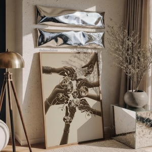 May include: A framed sepia-toned print depicts hands toasting with wine glasses. Above the print are two silver, rectangular wall decorations. A brass floor lamp and a mirrored side table are also visible in the room.