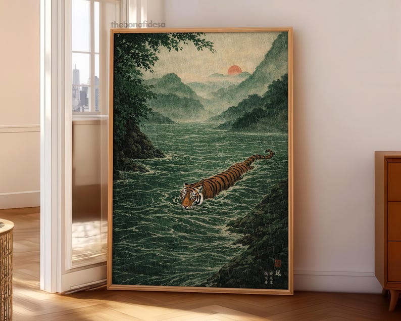 May include: A framed print depicting a tiger swimming in a river, in the style of Japanese art. The tiger has orange and black stripes. The background shows mountains, a red sun, and green foliage. The artwork is in a wooden frame.