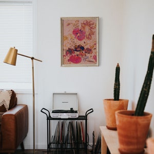 May include: A living room interior with a record player on a black metal stand with vinyl records. A framed floral print hangs on the wall above the record player. Two potted cactus plants are on a wooden shelf.