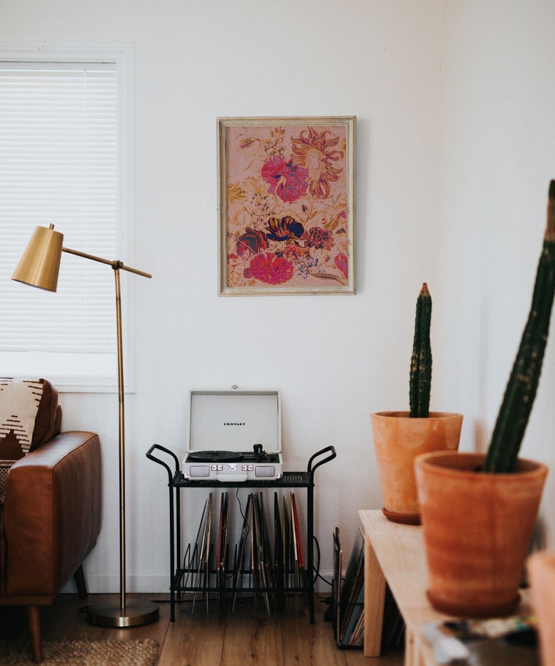 May include: A living room interior with a record player on a black metal stand with vinyl records. A framed floral print hangs on the wall above the record player. Two potted cactus plants are on a wooden shelf.