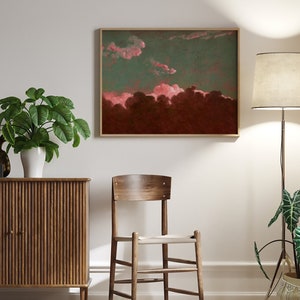May include: A framed abstract painting with pink and red clouds against a dark green and brown background. The painting is hanging on a white wall above a wooden cabinet and a wooden chair.