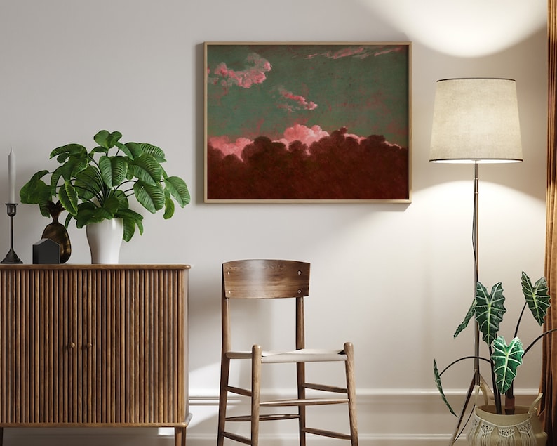 May include: A framed abstract painting with pink and red clouds against a dark green and brown background. The painting is hanging on a white wall above a wooden cabinet and a wooden chair.