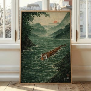 May include: A framed print depicting a tiger swimming in a river, set against a backdrop of mountains and a red sun. The artwork features a tiger with orange and black stripes, with green water and mountains in the background.