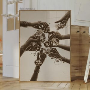 May include: Sepia-toned print of hands toasting with stemmed glasses. The image captures a celebratory moment, with multiple hands reaching towards each other, holding up the glasses. The artwork is framed in a light-colored wooden frame, adding a touch of elegance.