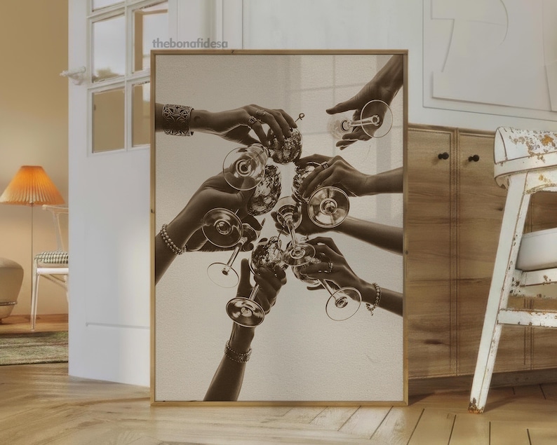 May include: Sepia-toned print of hands toasting with stemmed glasses. The image captures a celebratory moment, with multiple hands reaching towards each other, holding up the glasses. The artwork is framed in a light-colored wooden frame, adding a touch of elegance.