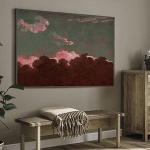 May include: A framed abstract painting with a dark green background and pink clouds. The painting is hanging on a light gray wall above a wooden bench with a beige throw blanket.
