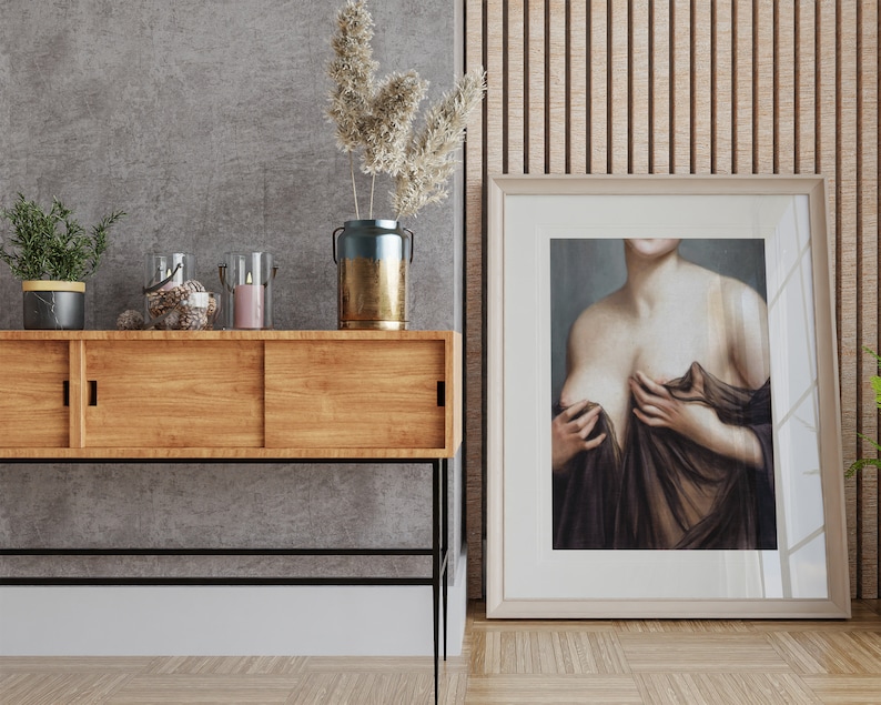 May include: A wooden console table with two sliding doors, a black metal frame, and black metal legs. The table is decorated with a vase of dried flowers, candles, and a decorative object. A framed painting of a woman in a brown dress is hanging on the wall behind the table.