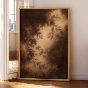 May include: A framed artwork featuring a sepia-toned image of tree branches and leaves. The artwork has a light brown wooden frame and is displayed in a room with natural light. The image has a soft, blurred effect, creating a sense of depth and tranquility.