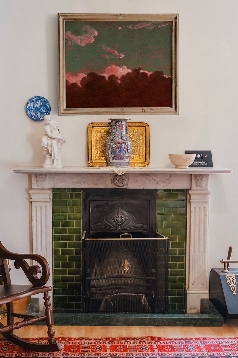 May include: A white marble fireplace with a green tiled surround and a black metal fire grate. A framed painting of a pink and green sky hangs above the fireplace. A white porcelain statue and a blue and white porcelain vase are on the mantel.