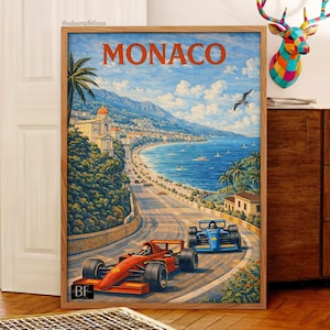 May include: Framed art print featuring a vintage-style illustration of Monaco. The artwork depicts a coastal road with race cars, the text "MONACO" in orange, and a scenic view of the sea and mountains. The print is in a wooden frame.