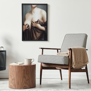 May include: A black and white checked armchair with a wooden frame and a beige throw blanket. The chair is in a living room setting with a wooden side table and a framed painting of a woman on the wall.
