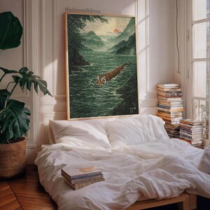 May include: A framed art print shows a tiger swimming in a river, with mountains and a sunset. The artwork is in a traditional Japanese style, with a natural colour palette. The print is displayed above a bed.