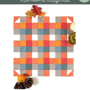 May include: A quilt pattern called "Seeing Plaid" by Sew Joyful Studio. The pattern features a plaid design in shades of orange, red, gray, and blue. The finished block size is 20 1/2 inches by 20 1/2 inches.