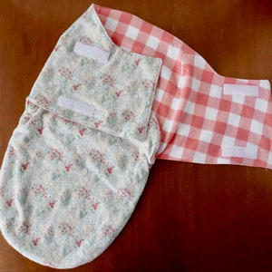 Peut inclure: Une gigoteuse pour b&eacute;b&eacute; avec un imprim&eacute; floral et un imprim&eacute; vichy rouge et blanc. La gigoteuse est dot&eacute;e de fermetures velcro.