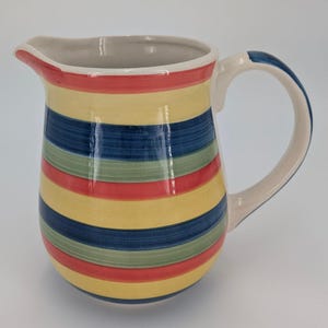 May include: A striped ceramic jug with a yellow, red, blue and green colour scheme. The jug has a wide base and a rounded body.