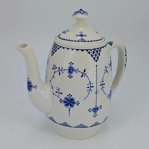 May include: A white ceramic teapot with a lid, spout, and handle. The teapot is decorated with blue floral patterns and a scalloped rim. The design includes a blue floral pattern around the body and on the lid.