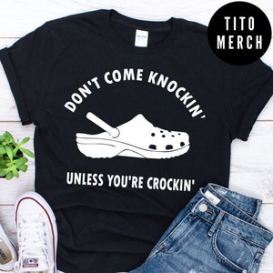 Könnte beinhalten: Schwarzes T-Shirt mit weißem Text, der "Don't come knockin' unless you're crockin'" lautet, und einer weißen Illustration eines Crocs.