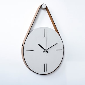 Könnte beinhalten: Eine weiße runde Uhr mit schwarzen Zeigern und römischen Ziffern. Die Uhr hängt an einem hellbraunen Lederband.