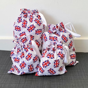 May include: Four white drawstring bags featuring a repeating Union Jack flag pattern in red, white, and blue. The bags are of varying sizes and have white drawstrings. The bags are made of fabric.