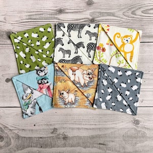 May include: Six fabric squares with different designs. The squares are green with white sheep, blue with a cat, brown with a pig, grey with white sheep, white with a zebra, and white with a monkey.