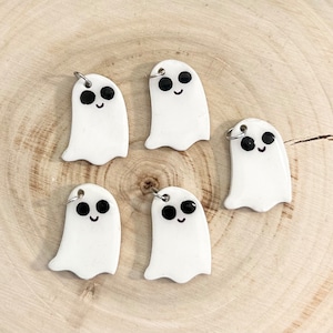Może przedstawiać: Pięć białych ceramicznych zawieszek w kształcie ducha z czarnymi oczami i uśmiechającym się ustami. Każdy duch ma srebrny pierścień do zawieszania.