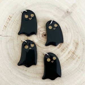 Puede incluir: Cuatro abalorios de fantasma de cerámica negra con ojos y sonrisas pintados en oro. Los abalorios tienen un lazo plateado para colgar.