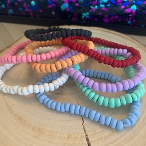 Könnte beinhalten: Ein Set aus acht bunten Haargummis aus Silikon. Die Haargummis sind in verschiedenen Farben, darunter Schwarz, Rosa, Orange, Rot, Lila, Hellblau und Mintgrün.