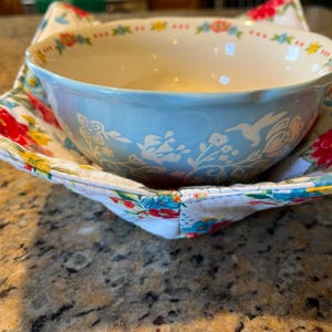 May include: A blue and white ceramic bowl with a floral design sits inside a white fabric bowl with a floral pattern. The fabric bowl has a red, yellow, and blue floral design.
