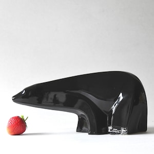 May include: A sleek, black bear sculpture with a glossy finish. A red strawberry with green leaves is positioned next to the bear. The bear has a modern, minimalist design.