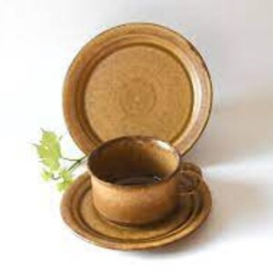 May include: A brown ceramic teacup and saucer set with a matching larger plate. The set has a rustic, earthy look.