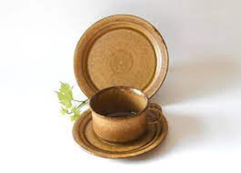 May include: A brown ceramic teacup and saucer set with a matching larger plate. The set has a rustic, earthy look.