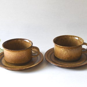 May include: Two brown ceramic teacups and saucers. The cups have a textured, speckled glaze. The saucers have a brown and white striped pattern.