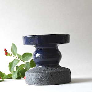 May include: A handcrafted ceramic candle holder with a two-tone design. The top section is a glossy navy blue, while the base has a textured, speckled gray finish. The holder has a unique, sculptural shape, and is suitable for home decor.