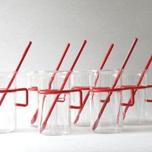 Peut inclure: Ensemble de six verres en verre transparent avec des poignées en métal rouge et des pailles rouges. Les verres sont disposés en rangée sur une surface blanche.